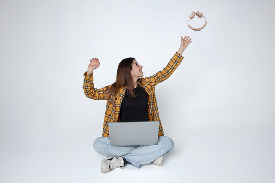 Mujer joven con port&aacute;til lanzando auriculares al aire sonriendo, concepto tecnolog&iacute;a y promoci&oacute;n