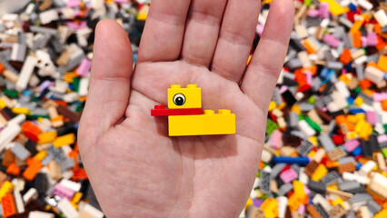 Fototapeta premium Small yellow and red LEGO plastic duck model held in a human hand over a background of scattered colorful building bricks on September 15, 2025 in Bangkok, Thailand.