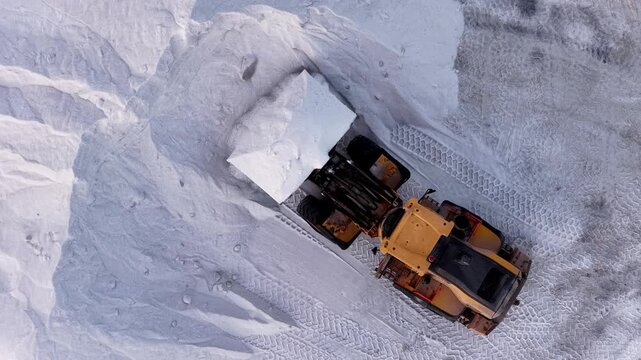 Aerial view of a yellow loader working with piles of white material, possibly salt, creating tire tracks in the area, Aigues-Mortes, Occitanie, France.