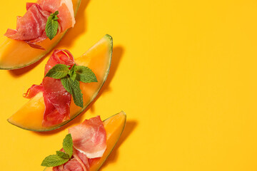 Fresh melon pieces with delicious prosciutto and mint leaves on yellow background © Pixel-Shot