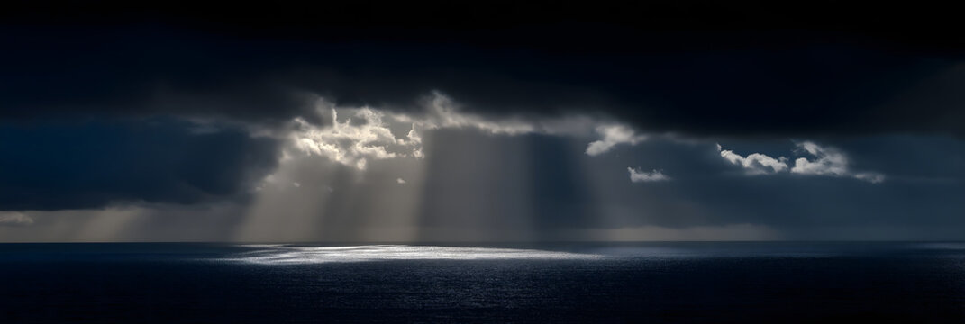 sunbeam slicing through heavy rain clouds over ocean horizon dramatic minimal stormscape