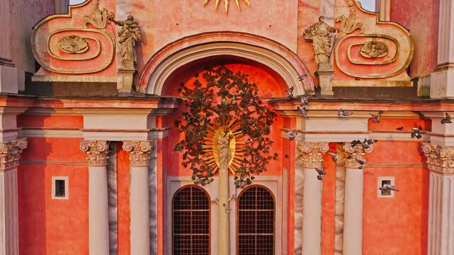 Flock of pigeons bursts upward before glowing Święta Lipka basilica at dusk