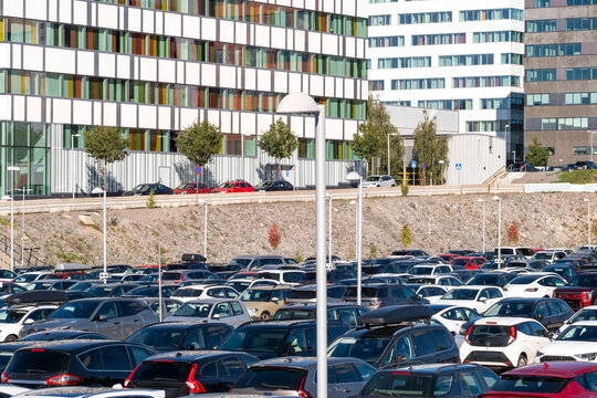 Parking full of cars and traffic in an urban transport commute beside buildings with flags in Stockholm Sweden under clear sky
