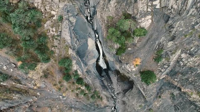 Aerial view of a narrow canyon with a flowing river. Surrounding rocky terrain features patches of green trees and shrubs.