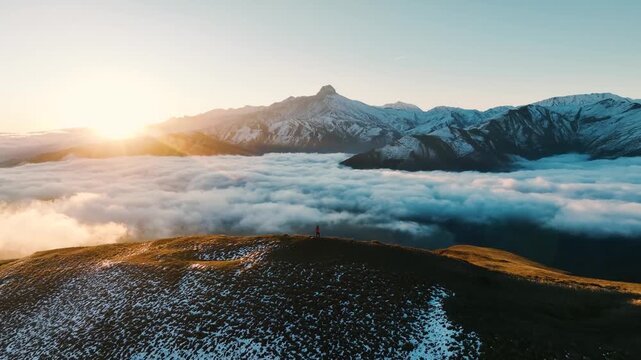 A breathtaking sunrise over snow-capped mountains and a sea of clouds. The landscape features rolling hills and a clear sky, creating a serene atmosphere.