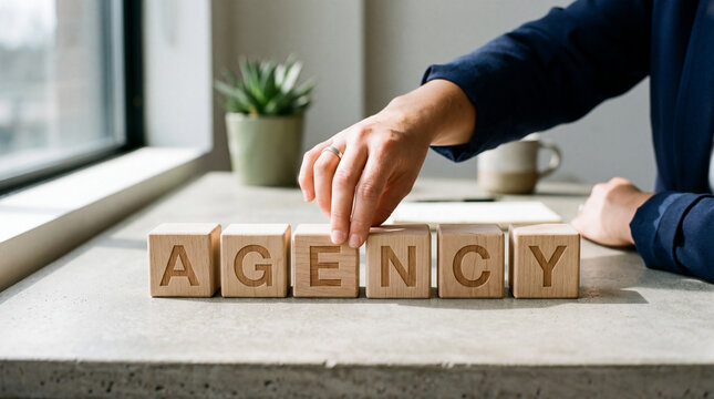 Hand arranging wooden blocks spelling AGENCY on desk concept