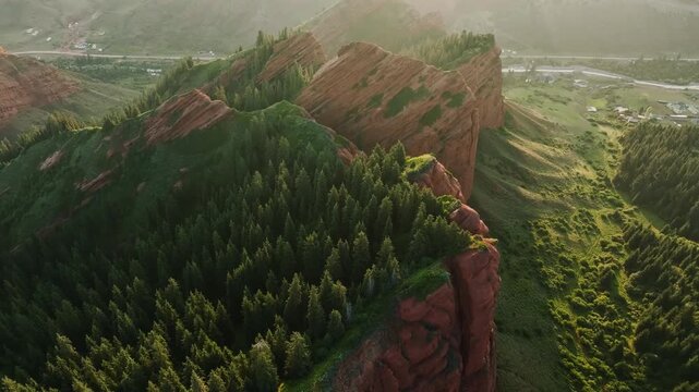 Aerial view of rugged red rock formations surrounded by lush green trees and a winding river in the valley below. Natural landscape with vibrant colors.