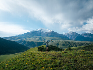 Woman open arms to snowcapped mountain on sunset grassland mountain top