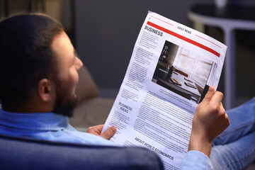 Naklejka premium Young man reading newspaper at home in evening, closeup