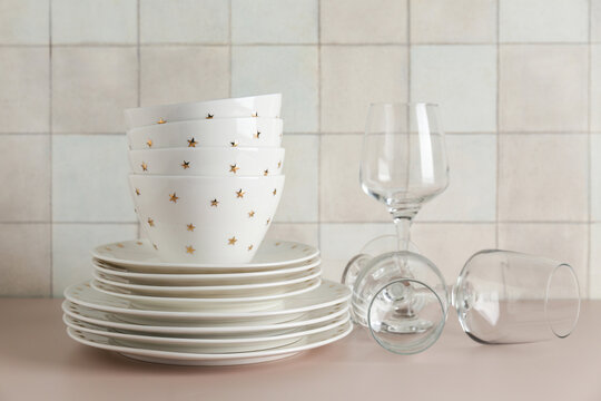 Clean glasses with plates, bowls and napkin on beige table against tile wall