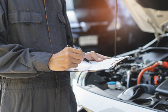 Auto check up and car service shop concept. Mechanic writing job checklist to clipboard to estimate repair quotation to client at workshop garage.