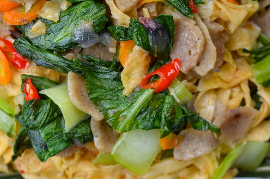 Capcay or stir fried mixed vegetables with meatballs and eggs. Traditional Asian healthy dish served on a green plate with wooden table background.