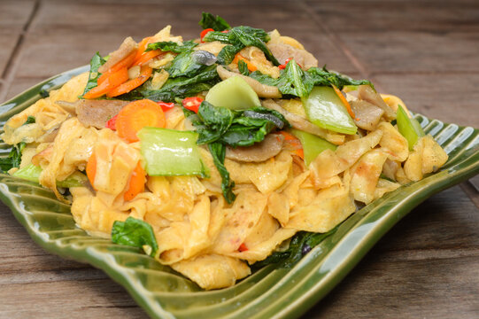 Capcay or stir fried mixed vegetables with meatballs and eggs. Traditional Asian healthy dish served on a green plate with wooden table background.