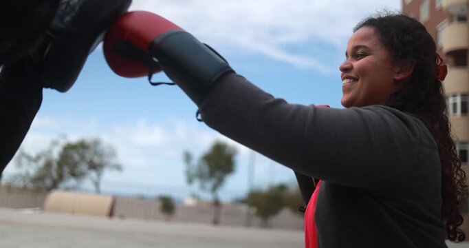 Curvy latin girl having fun during boxing exercise with personal trainer outdoor - Plus size people, sport and diet concept 