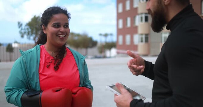 Curvy african american woman talking with her personal trainer while checking workout plan on tablet outdoor - Sport and healthy lifestyle for plus size people concept