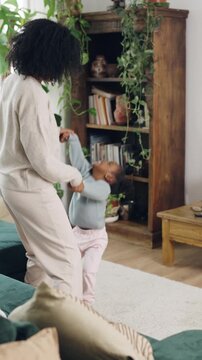 Happy black mother and her cute toddler daughter having fun dancing together. Loving family enjoying a playful moment in their cozy living room. Vertical