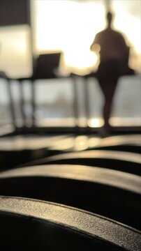 Blurred silhouette running on treadmill in gym at sunset