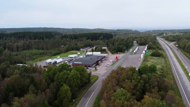 Aerial drone shot of highway rest stop with service station, parking area, trucks and cars beside the E6 road in Hallandsasen, Sweden surrounded by forest landscape