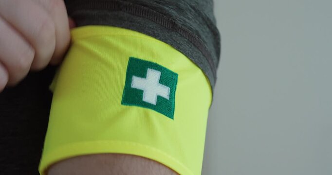 Close-up of a yellow first aid armband with a green medical cross worn on the upper arm, representing emergency preparedness, healthcare responsibility, and community safety support.