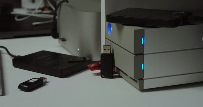 Close-up of external hard drives and USB sticks connected to a desktop server with active indicator lights, representing data backup, cloud synchronization, and digital storage management.