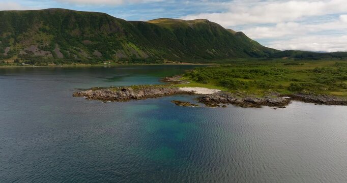 Aerial flyover establishing of rocky shoreline and calm fjord near Stokmarknes Norway under summer light