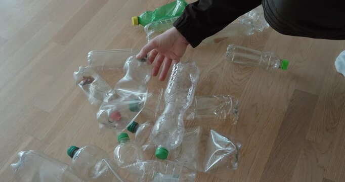 Hand gathering empty plastic bottles from the floor, highlighting waste collection, deposit return systems, and environmentally responsible household recycling.