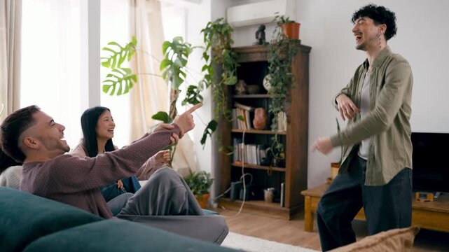 Cheerful group of friends enjoying a game of charades in the living room. One man acts out a word while his friends laugh and guess