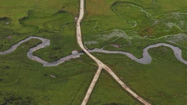 Aerial view of the winding river cutting through the lush green Phobjikha Valley, alongside a converging road network, creating a serene landscape, Nubding, Bhutan.
