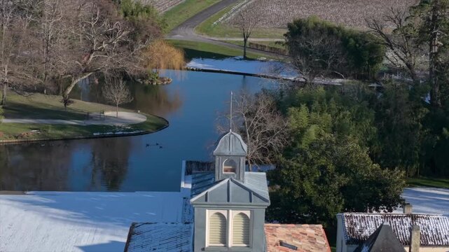 Chateau Lagrange, France - 06 January 2026: Aerial view of a serene lake reflecting the sky, framed by bare trees and green bamboo, with a vineyard backdrop.