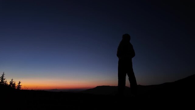 Man with smartphone photographing and observing mountain landscape in dawn - dusk - twilight.