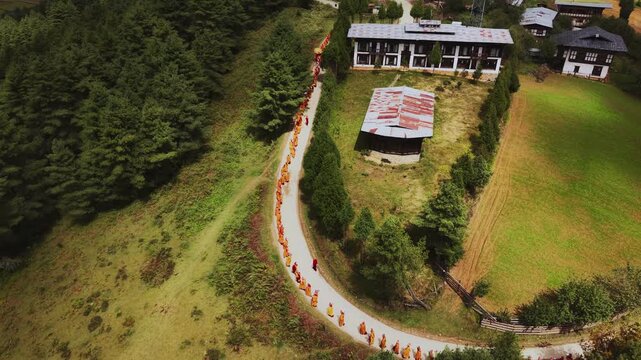 Nubding, Bhutan - 21 September 2025: Aerial view of monks walking along a winding road, contrasting against the lush green landscape of Phobjikha Valley.