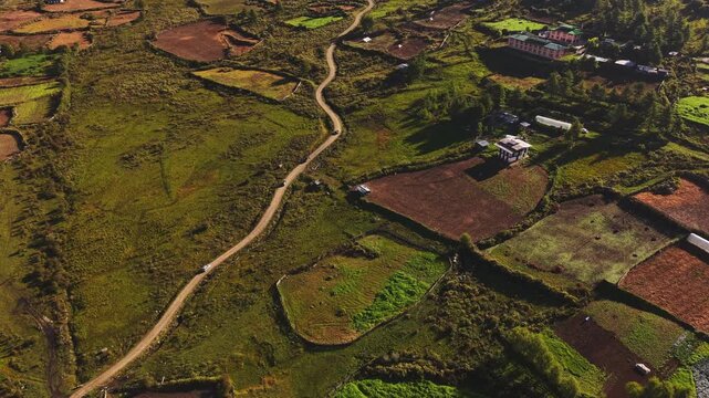 Aerial view of a winding road through the Phobjikha Valley, showcasing a tapestry of green meadows and cultivated fields, Nubding, Bhutan.