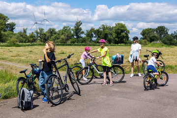 Naklejka premium Smiling happy family enjoy riding bikes at European park countryside on bright sunny day. Mom with children cycling at country landscape. Kid use safety helmets bicycle. Healthy lifestyle activities