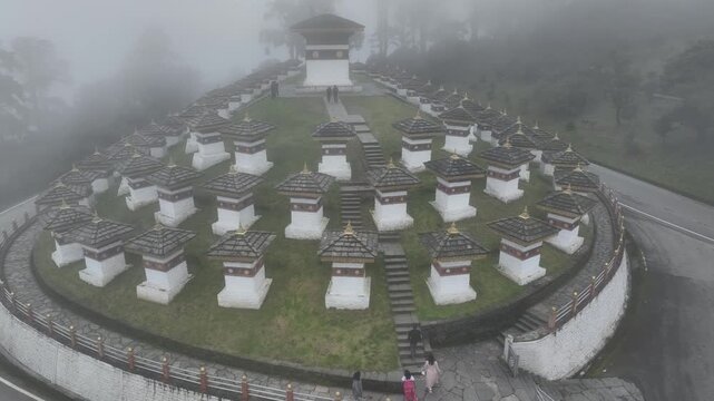 Aerial view of the Dochula Chorten shrouded in mist, with rows of white and brown stupas and a central monument, Dochula Chorten, Thimphu, Bhutan.