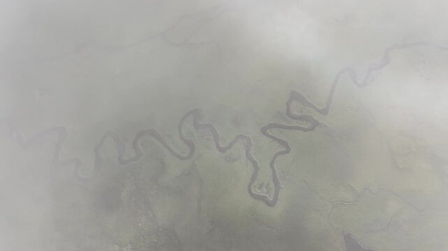 Aerial view of a winding river snaking through a valley, contrasting the dark water against the surrounding landscape, Phobjikha Valley, Wangdue Phodrang, Bhutan.