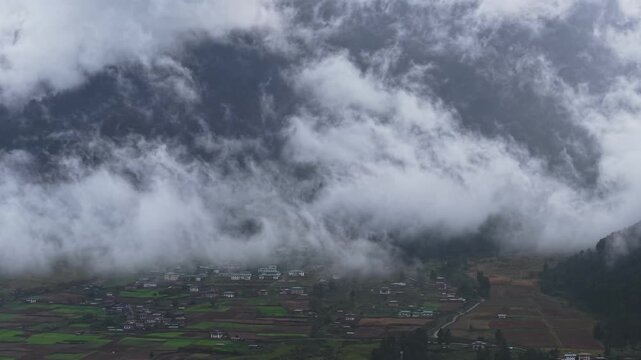 Aerial view of Phobjikha Valley shrouded in mist, with patches of green fields and houses emerging from the ethereal fog, Nubding, Bhutan.