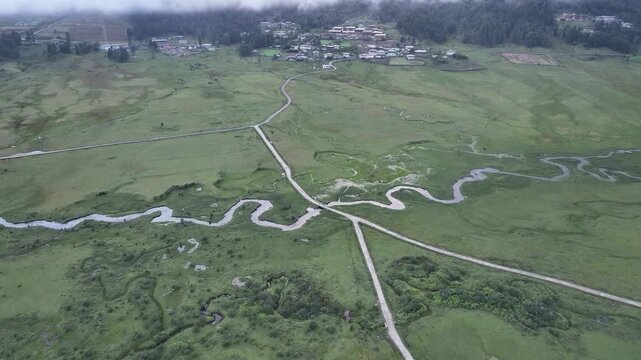 Aerial view of a winding river flowing through the lush, green Phobjikha Valley, contrasted by the village structures, Phobjikha Valley, Wangdue Phodrang, Bhutan.