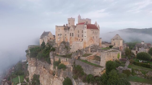 Beynac-et-Cazenac, France - 12 September 2025: Aerial view of Chateau de Beynac, a medieval fortress shrouded in mist atop a cliff, its stone walls blending with the fog.