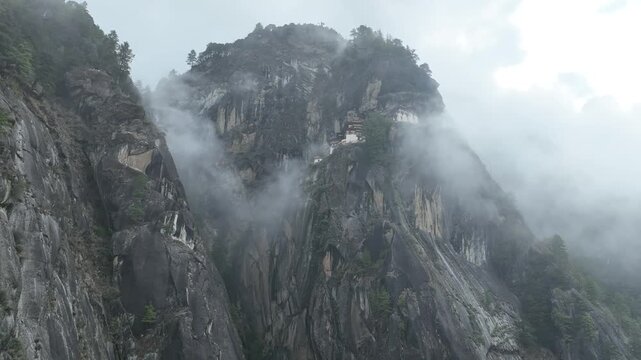 Aerial view of the Taktsang Tiger's Nest clinging to the cliffside amidst swirling clouds, creating a mystical and ethereal scene, Taktsang, Paro, Bhutan.