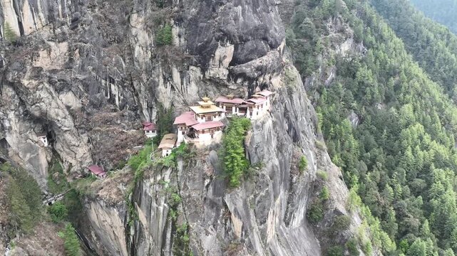 Aerial view of the Tiger's Nest Monastery perched dramatically on a cliffside, a vivid contrast against the rugged terrain, Taktsang, Paro, Bhutan.