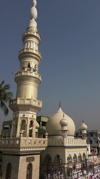 Aerial view of devotees gathered near a mosque with a tall minaret and white dome, basking in the sunlight, Malda, West Bengal, India.