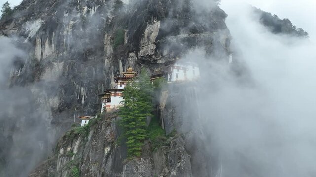 Aerial view of the iconic Tiger's Nest Monastery clinging to the cliffside, shrouded in mist and clouds, a fusion of nature and architecture, Paro, Bhutan.