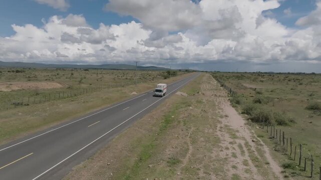 Aerial view of a long road cutting through the arid landscape under a cloudy sky, with green and brown tones, Narok, Narok, Kenya.
