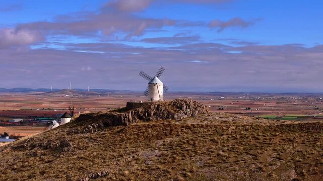 Aerial view of white windmills standing majestically atop a hill overlooking the expansive landscape under a blue sky, Consuegra, Castile-La Mancha, Spain.