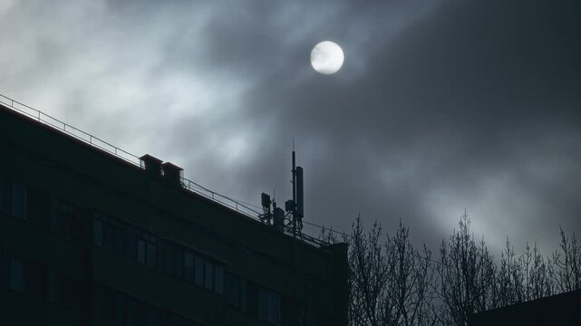 Night Sky With Moon And Clouds. Lunar Disk Over City Roof With Dramatic Cloud Formations And Silhouettes