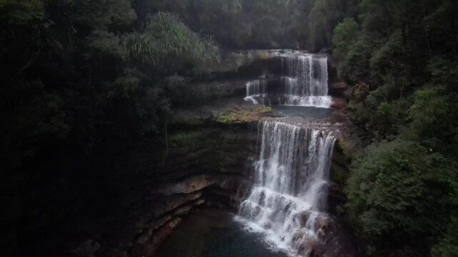 Aerial view of a tiered waterfall cascading into a dark pool surrounded by lush green trees and dark rocks, Shillong, Meghalaya, India.