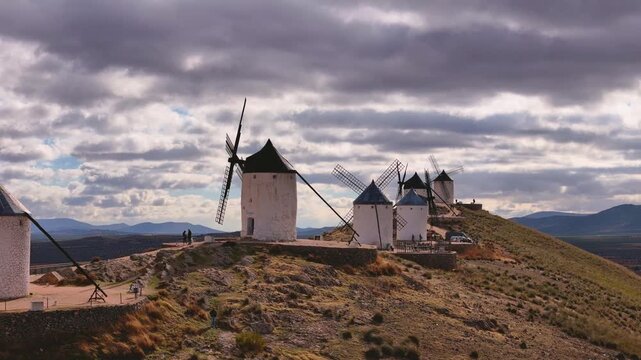 Aerial view of the iconic windmills standing majestically atop a hill, their white walls contrasting against the dramatic cloudy sky, Consuegra, Castile-La Mancha, Spain.
