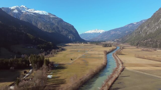 Aerial view of the winding Drau river cutting through the valley with snow-capped mountains under a clear sky, Greifenburg, Carinthia, Austria.