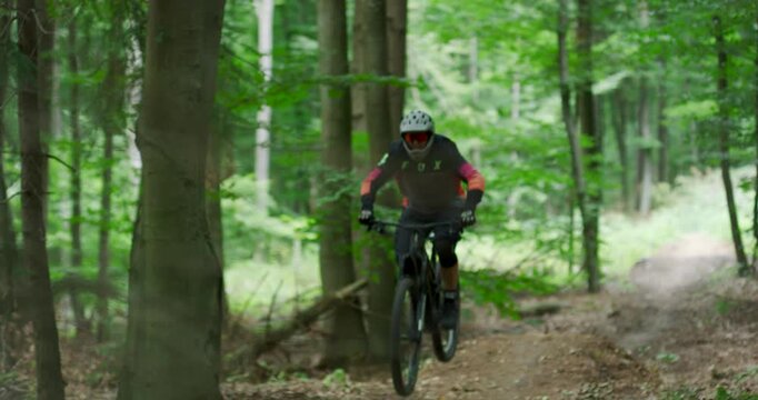 Title: Front View of Professional Mountain Biker Jumping Mid-Air on a Forest Trail, Extreme Action Shot of MTB Rider Performing Stunt in Green Summer Woods with Cinematic Lighting and Motion