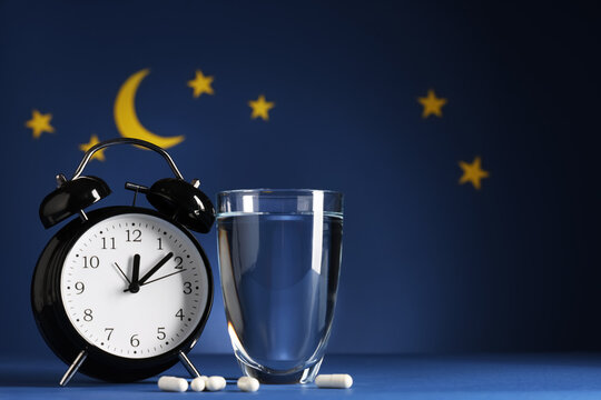 Melatonin pills with glass of water, alarm clock and stars on blue background